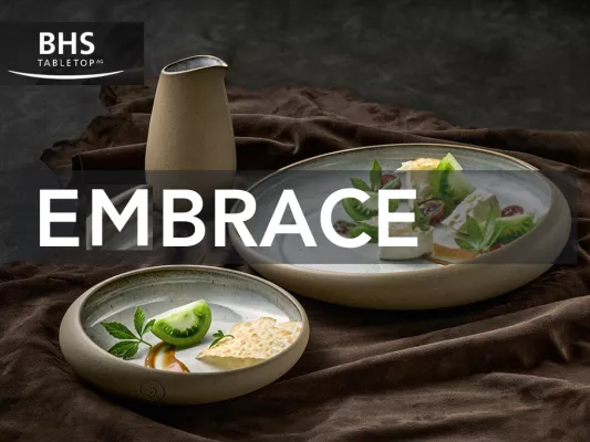 The picture shows two elegantly arranged dishes in beige bowls on a dark cloth. A beige jug in the background. Text: “BHS Tabletop AG - Embrace”.
